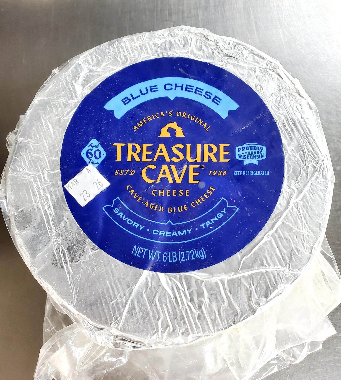 Round blue cheese wheel with 'Treasure Cave' label on a metallic surface