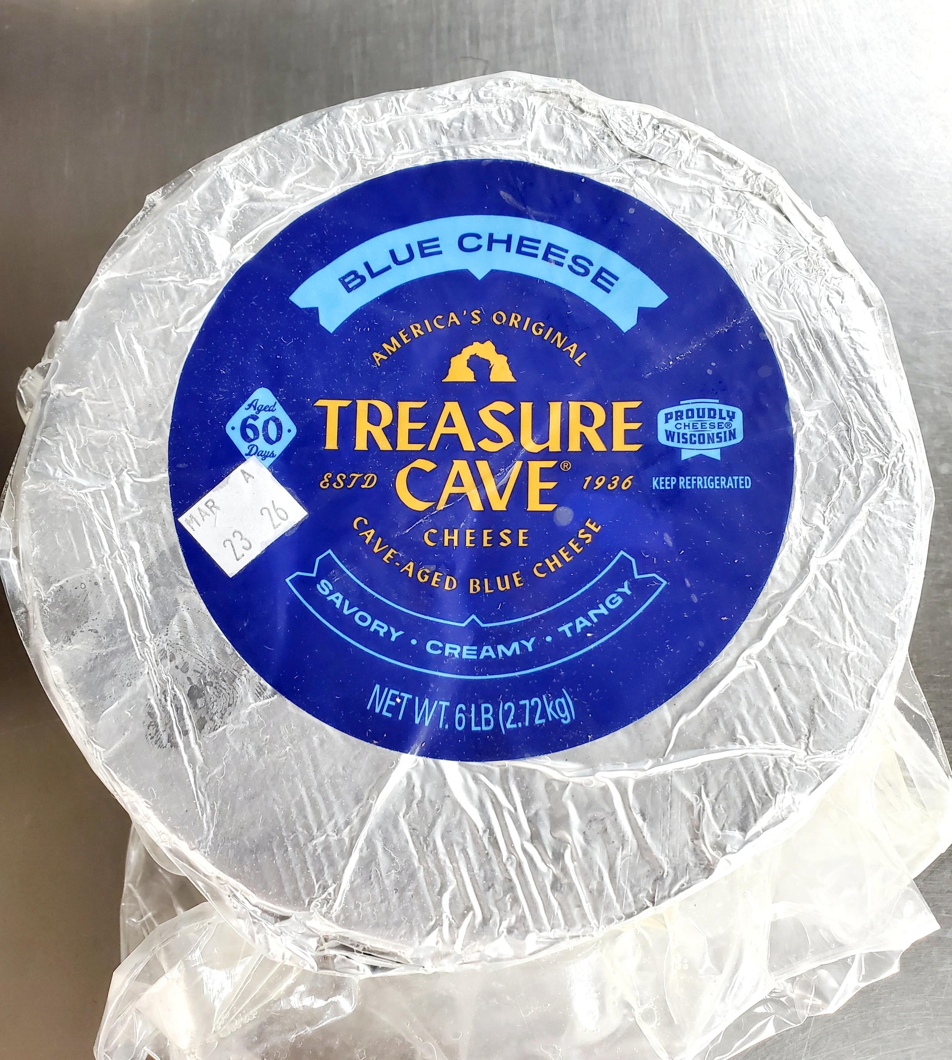 Round blue cheese wheel with 'Treasure Cave' label on a metallic surface